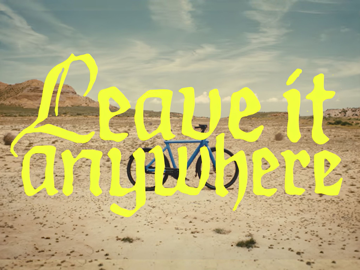 A blue VanMoof e-bike parked alone in a barren desert landscape with bold, jagged yellow text reading "Leave it anywhere" overlaid across the scene.