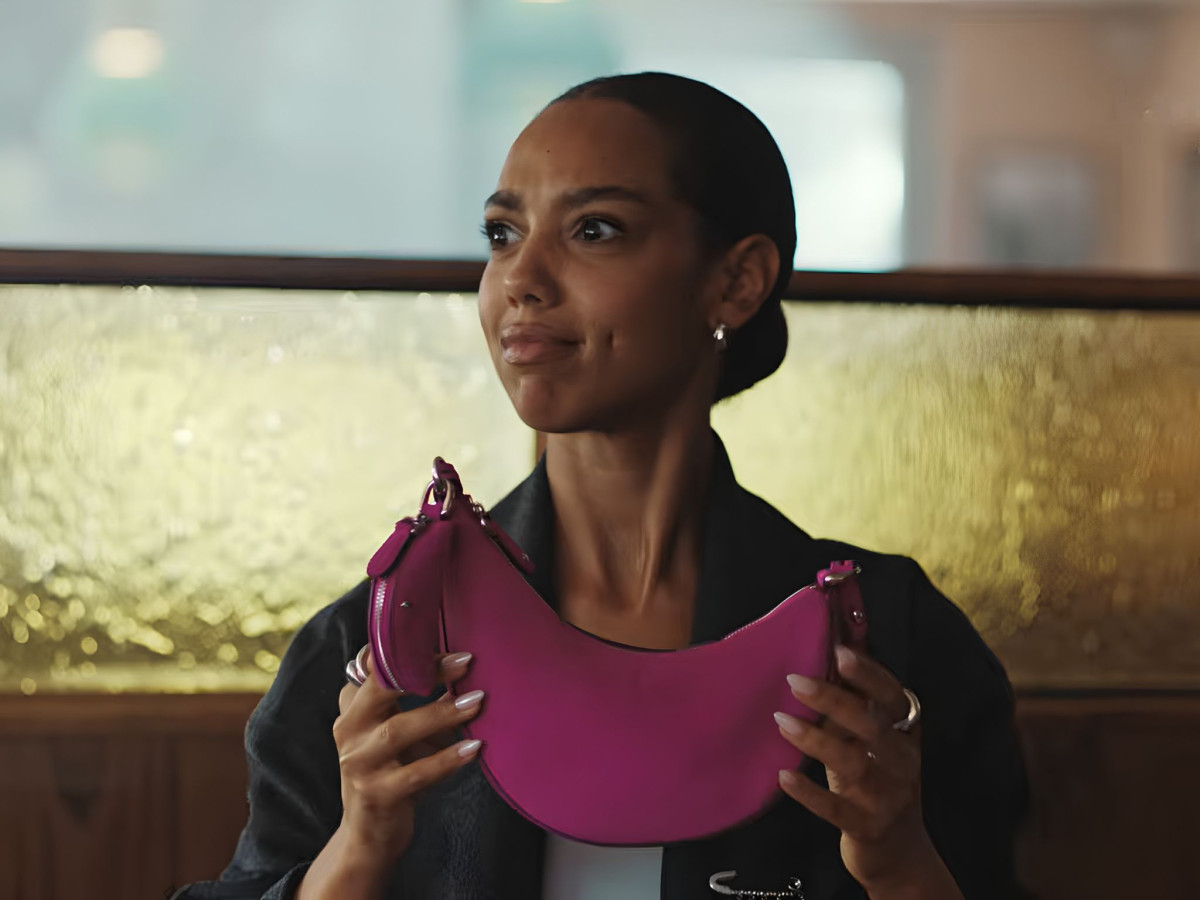 Woman holding a pink curved shoulder bag.