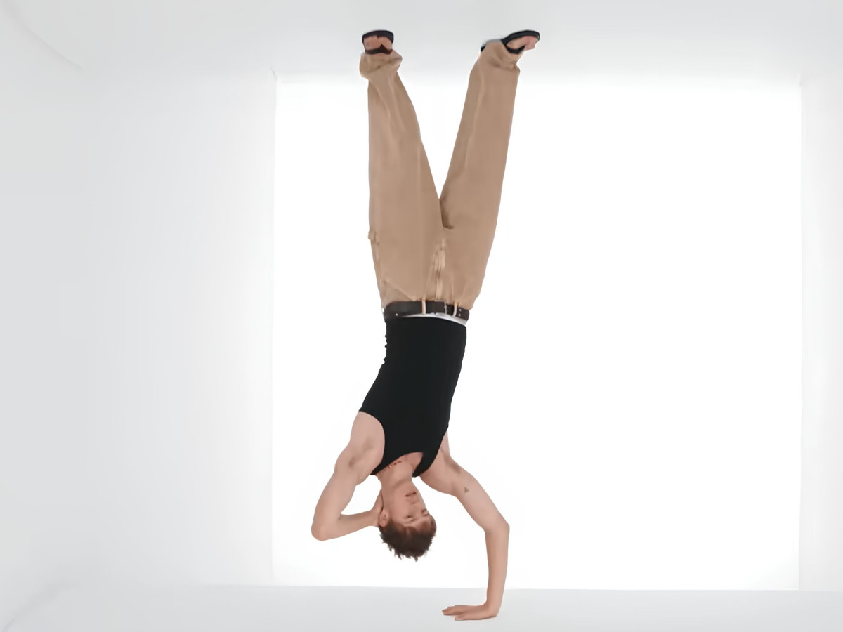 Man doing a one-handed handstand in white room.