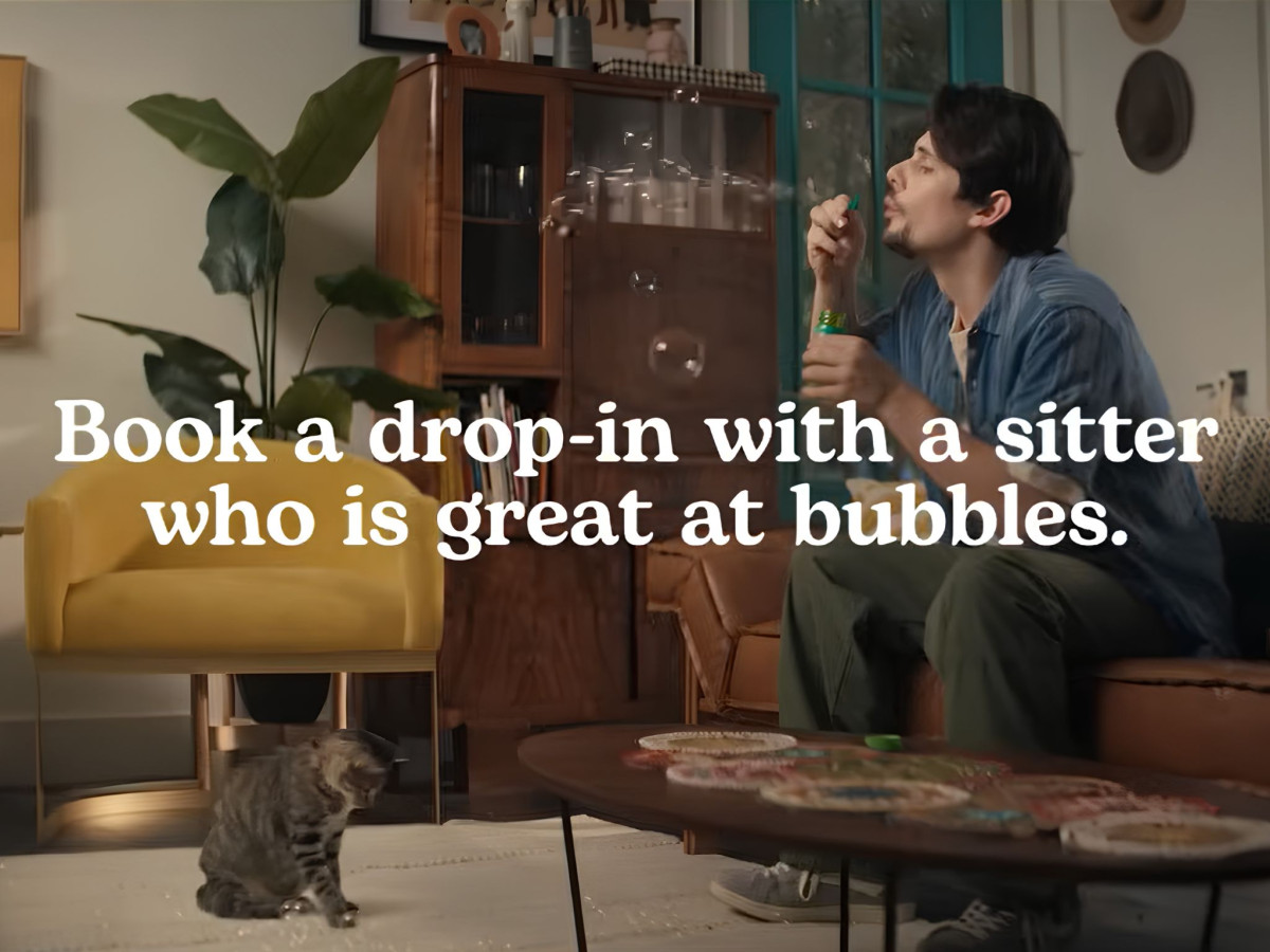 Man on couch blowing bubbles for a cat.