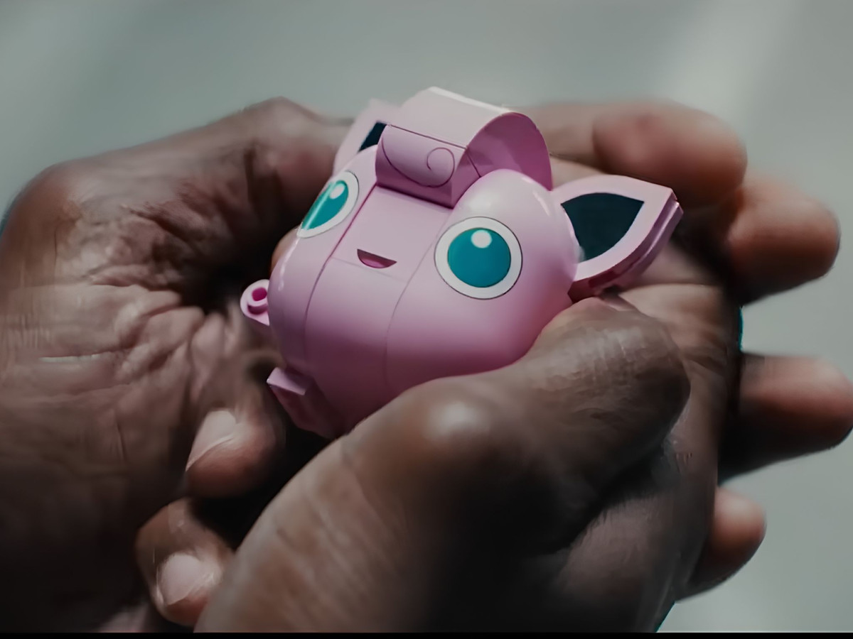 Large hands gently holding a pink LEGO Jigglypuff figure.
