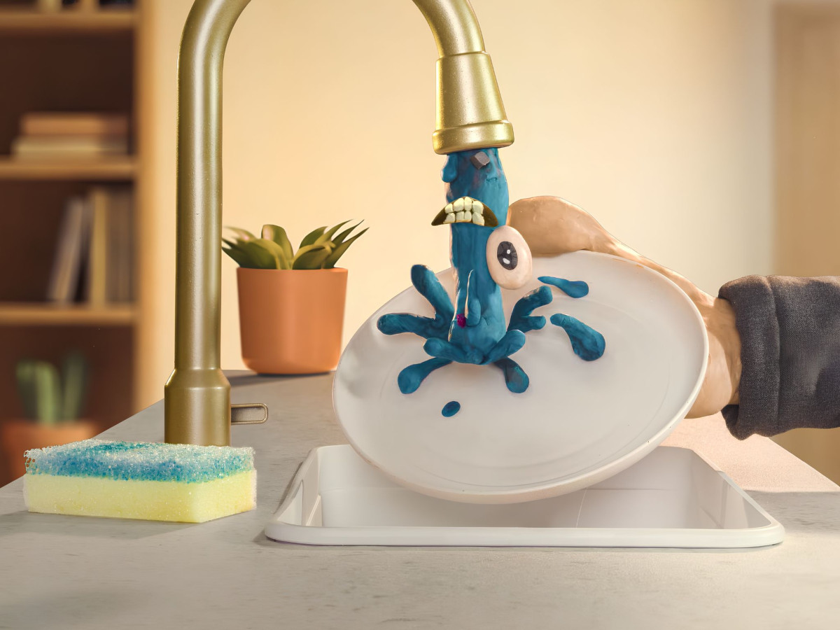 Blue clay monster splashing onto plate under kitchen faucet.