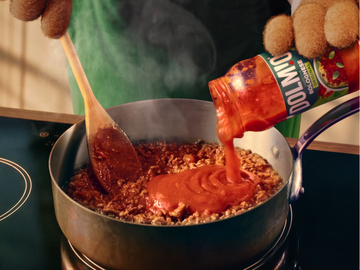 Puppet hands pouring Dolmio sauce into a pan of meat.