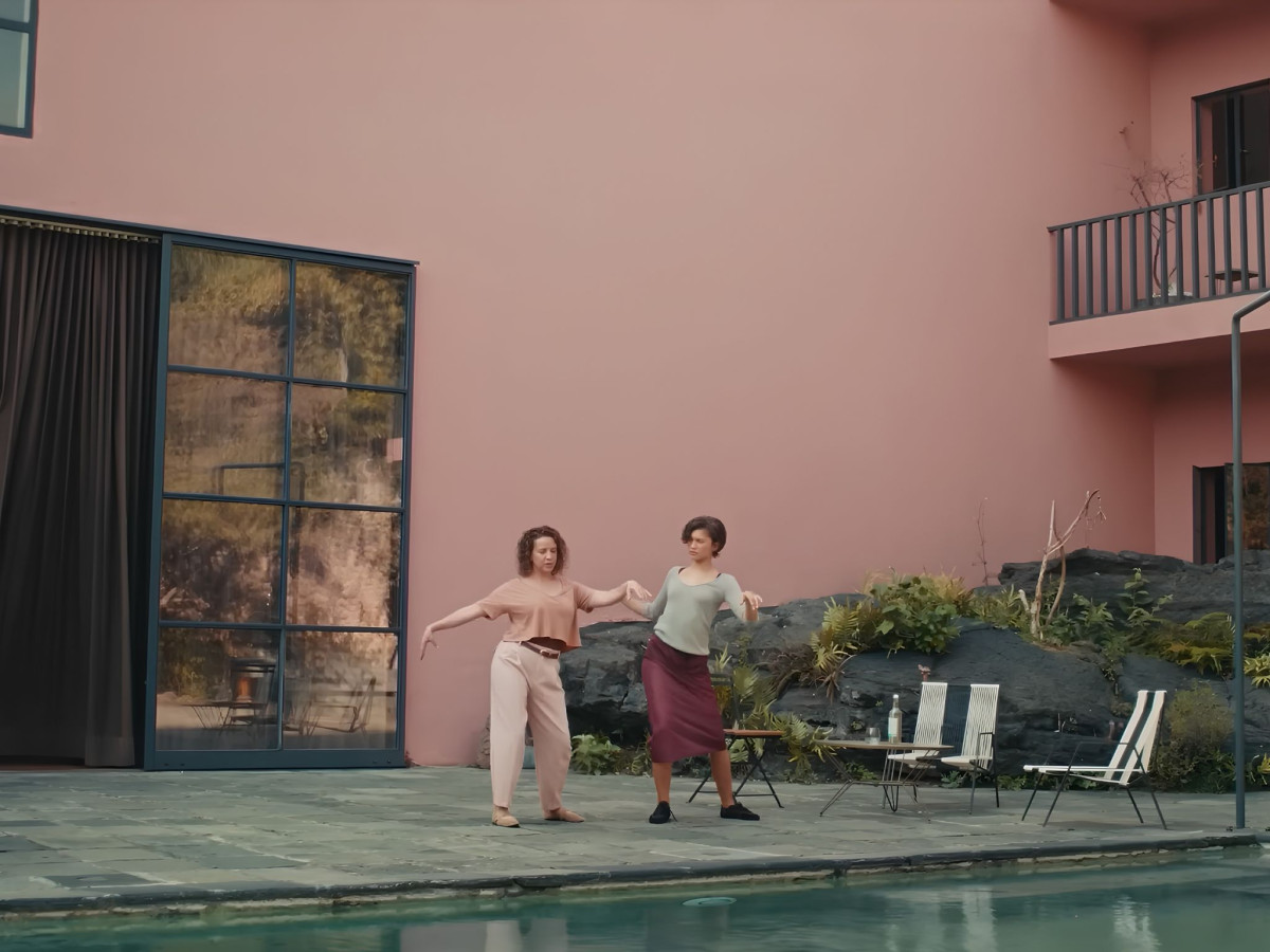 Two women dancing by a pool and pink wall.