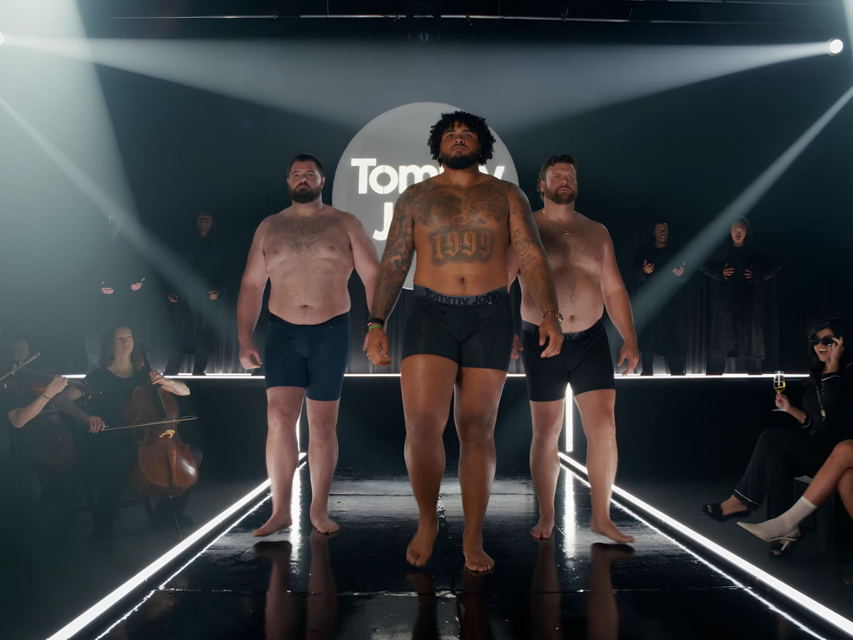 Three large men wearing black underwear walking a fashion runway.