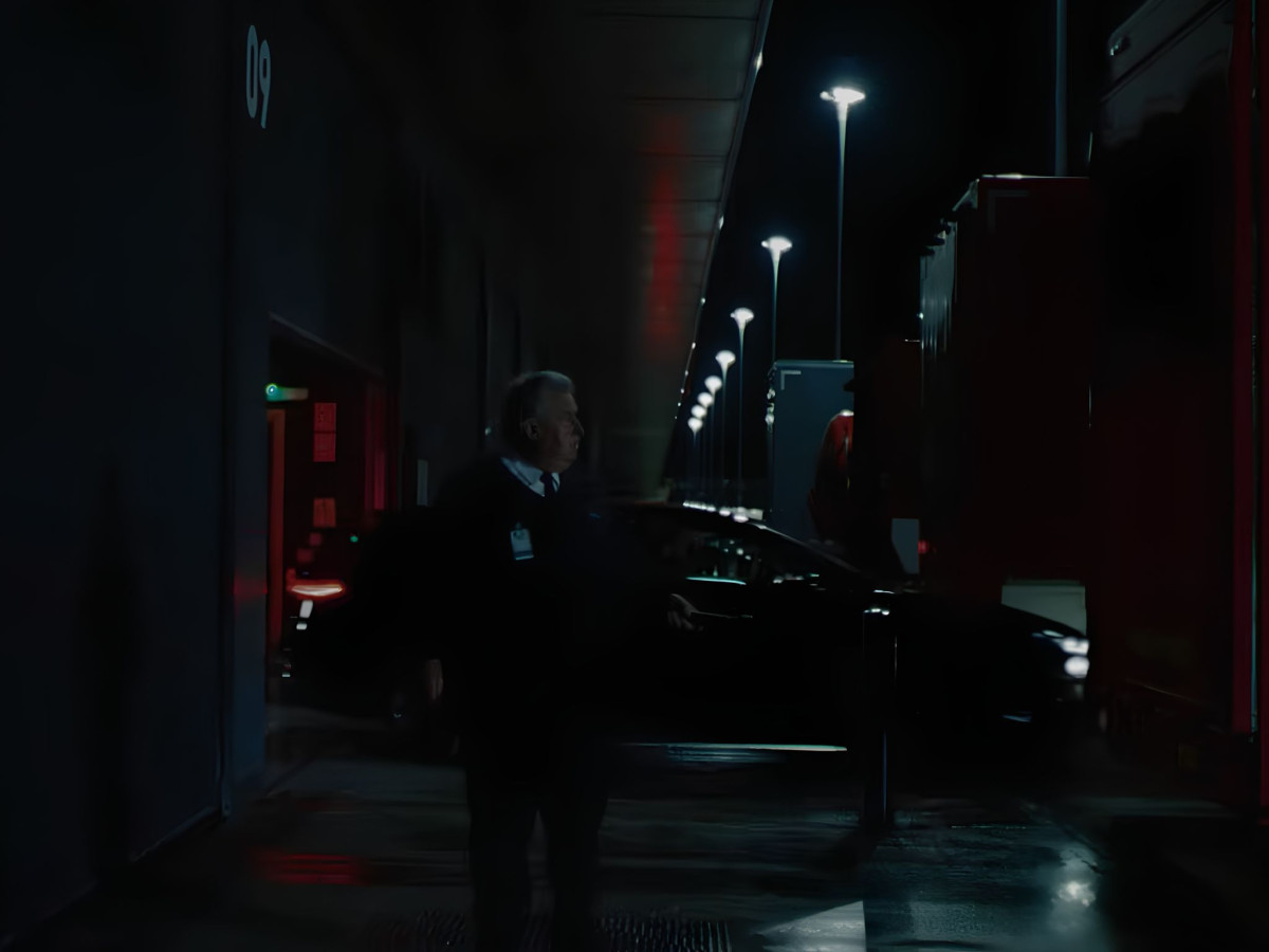 Security guard walking past a dark Audi at night.