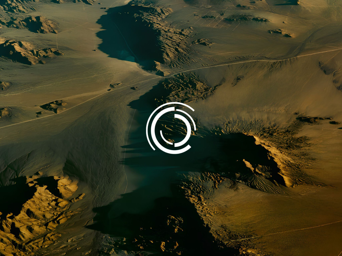 Circular arc logo emblem overlaid on an aerial desert landscape.