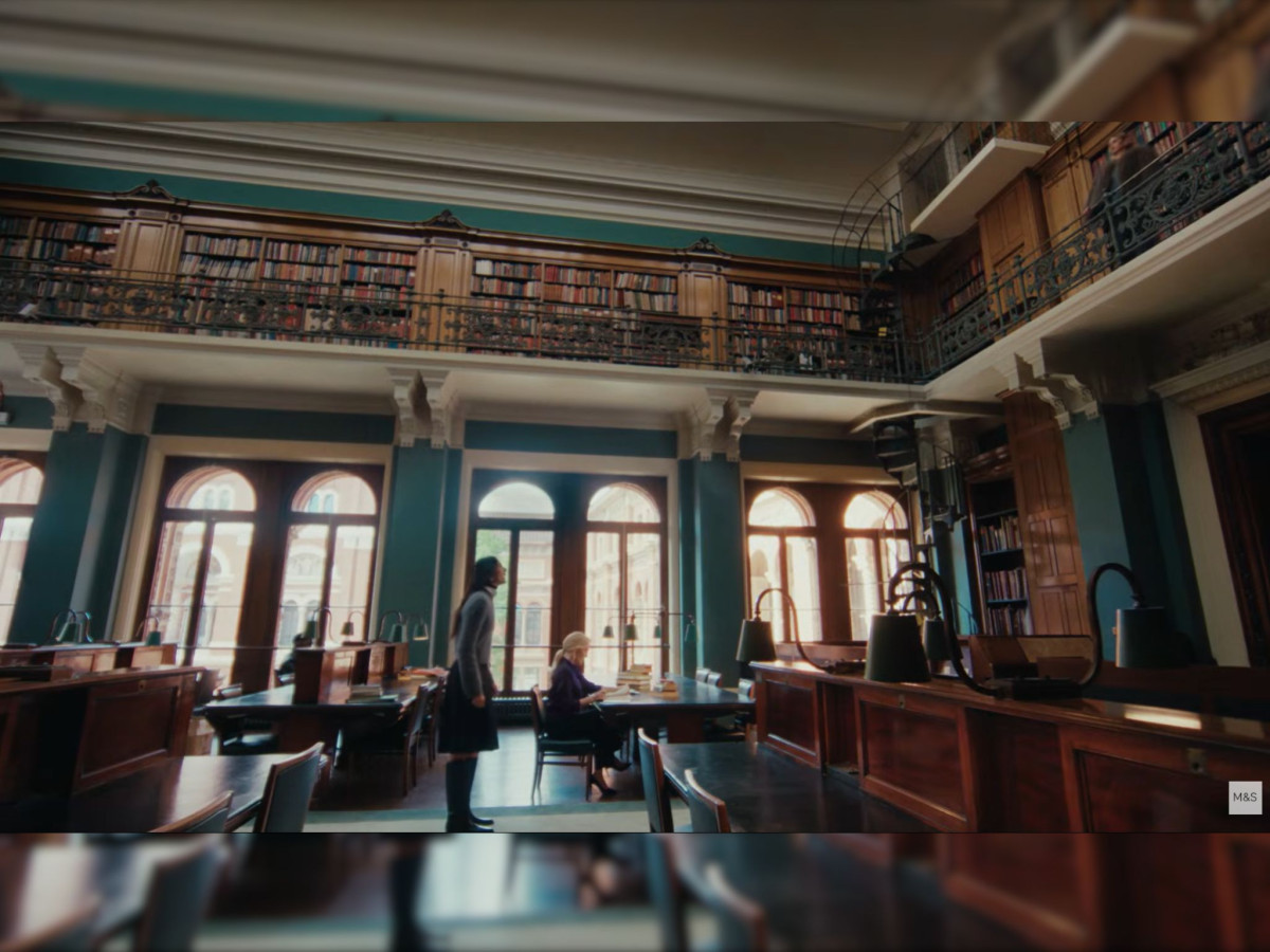 Two women at a desk in a grand library.