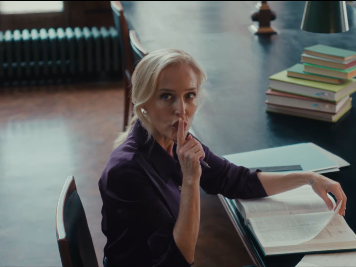Gillian Anderson in a purple shirt shushing someone.