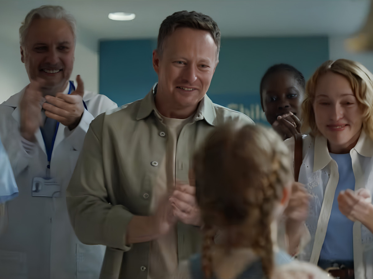 Smiling parents and doctor clapping for a young girl.