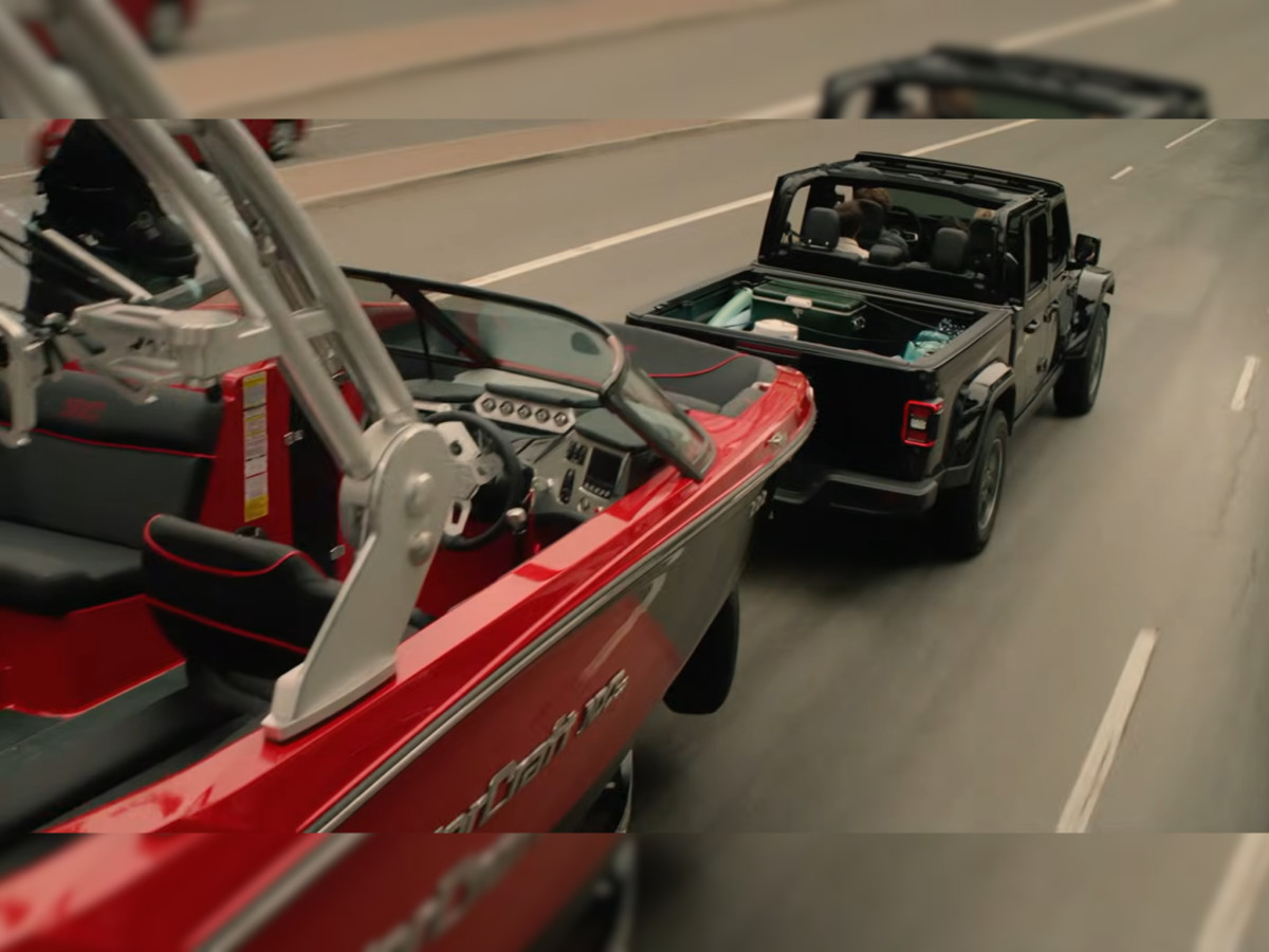 Black Jeep pickup truck towing a red speedboat.