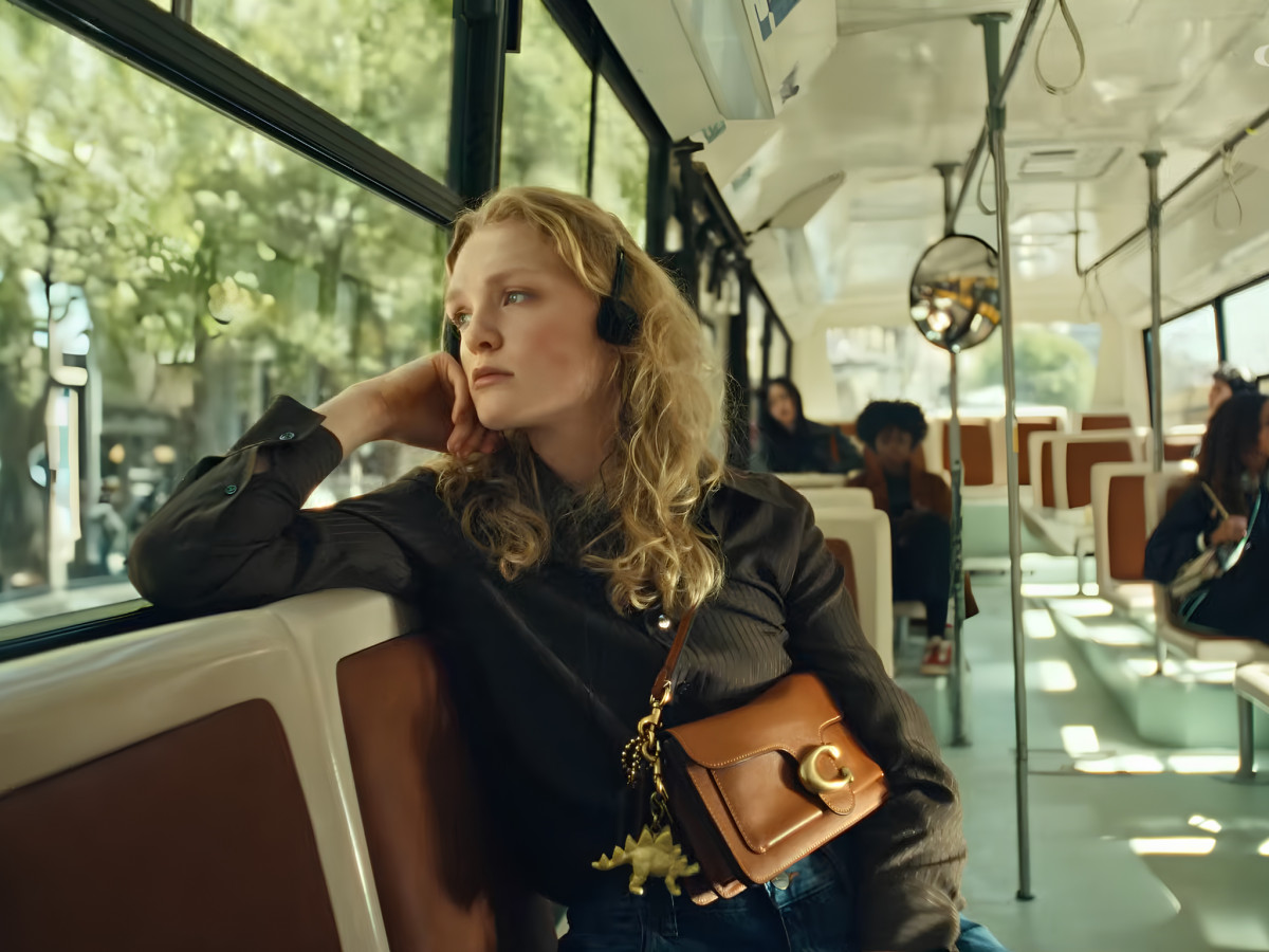Elle Fanning sitting inside a tour bus holding a Coach handbag.