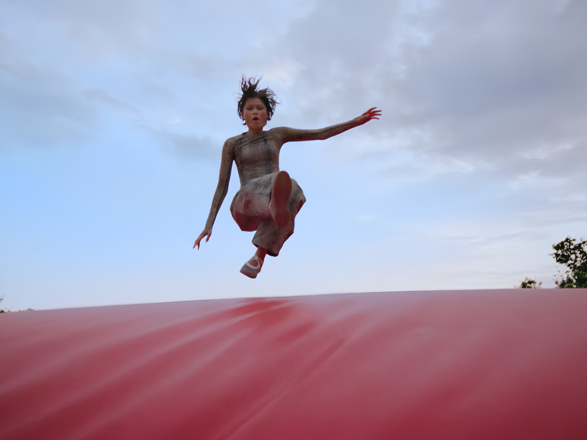 Zendaya leaping mid-air onto a red stunt crash pad.