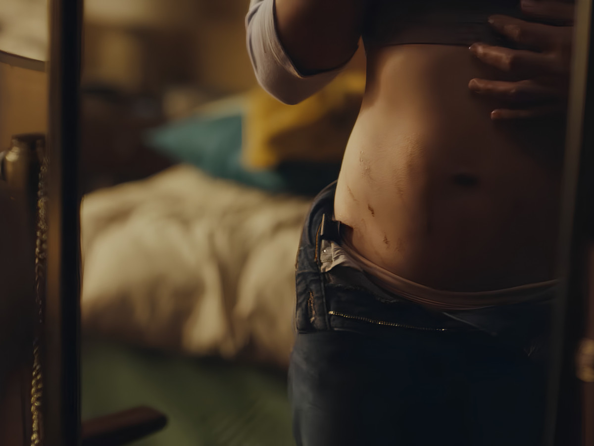Woman viewing her bare postpartum stomach in a mirror.