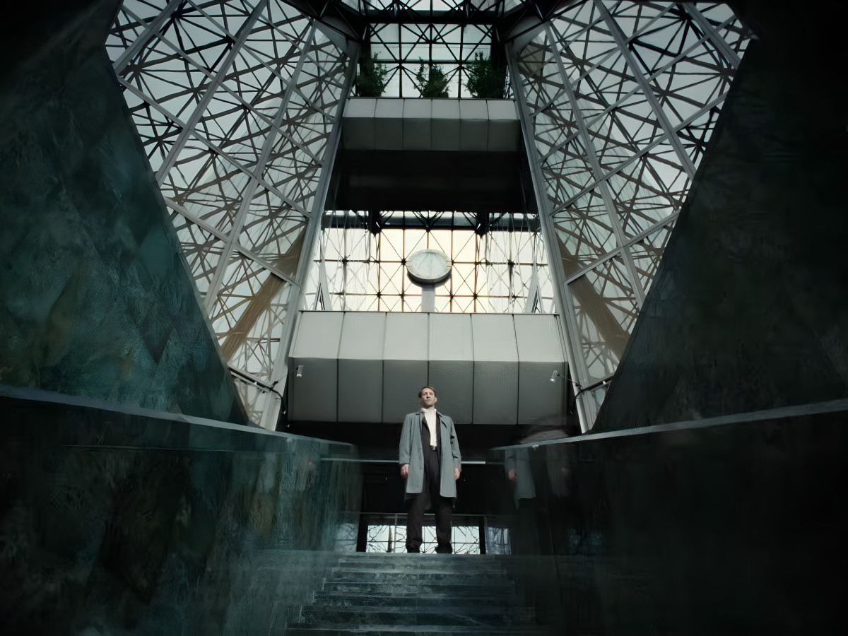Man standing on a staircase inside a building with a geometric glass ceiling and a prominent clock.