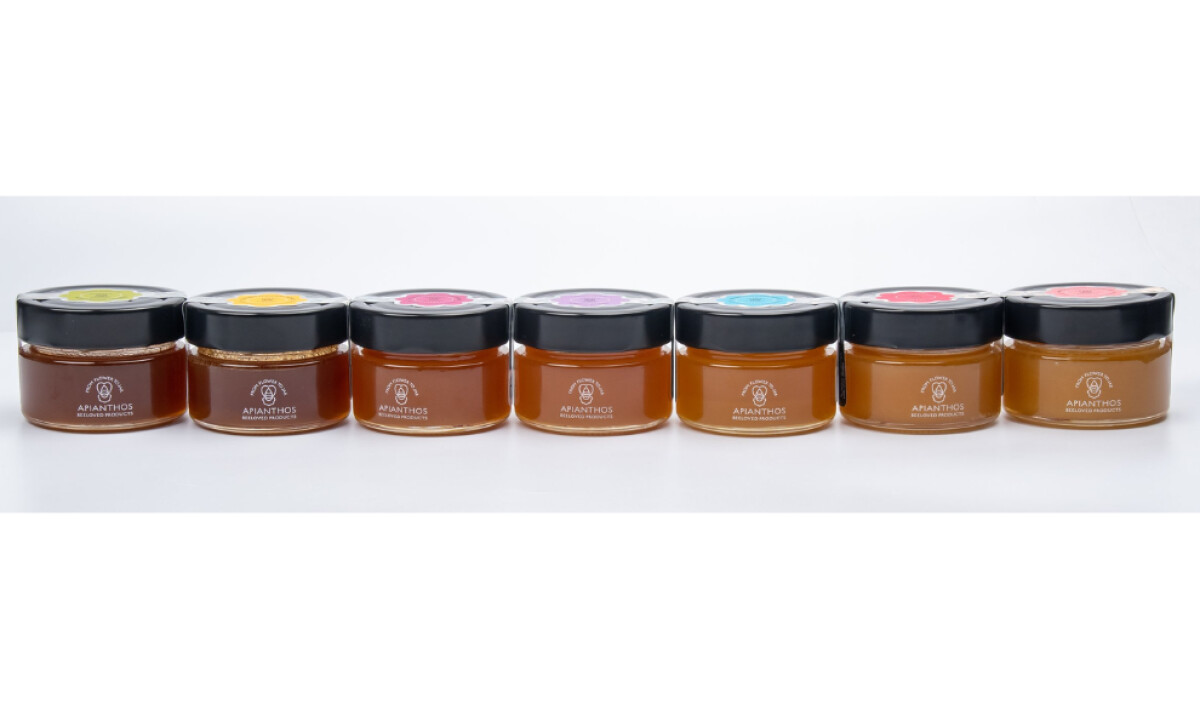 Row of seven Apianthos Organic honey jars with different colored lid by Appios