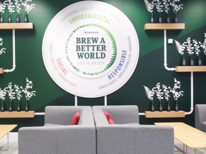 Modern lounge area with a large, circular Heineken "Brew a Better World" graphic on a dark green wall by Coolgrey.