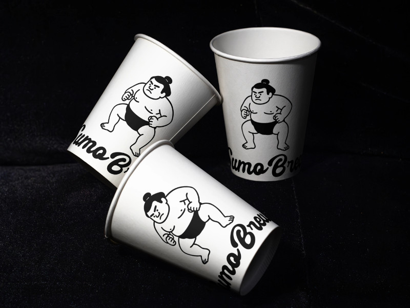 Sumo Brew coffee cups with playful sumo wrestler illustrations on black background
