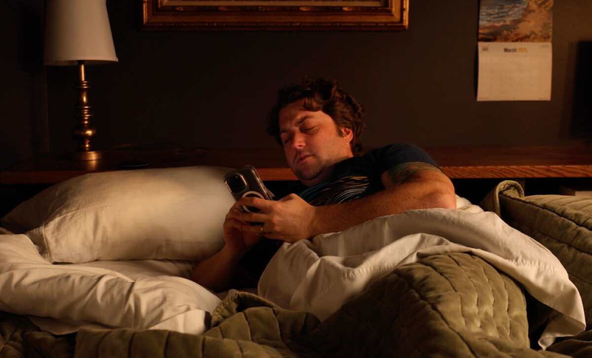 A man lying in bed, looking at his phone.