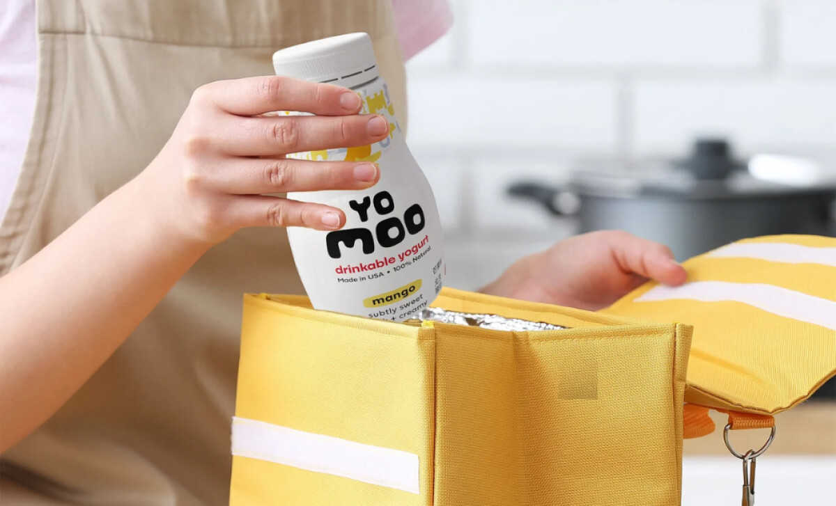 A person places a bottle of Yomoo mango yogurt into a lunch bag by BLC Design.