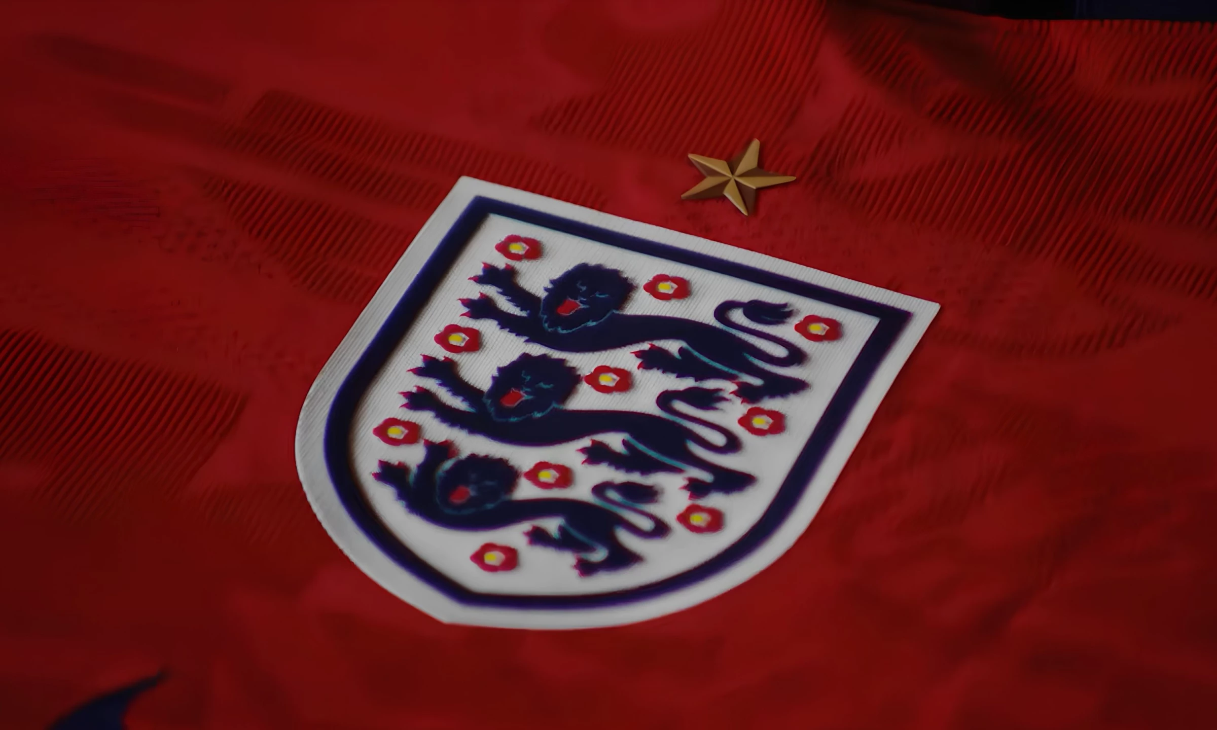 england-lions-crest England's Three Lions crest on a red away kit — three navy lions, ten Tudor roses, one gold star, white shield.