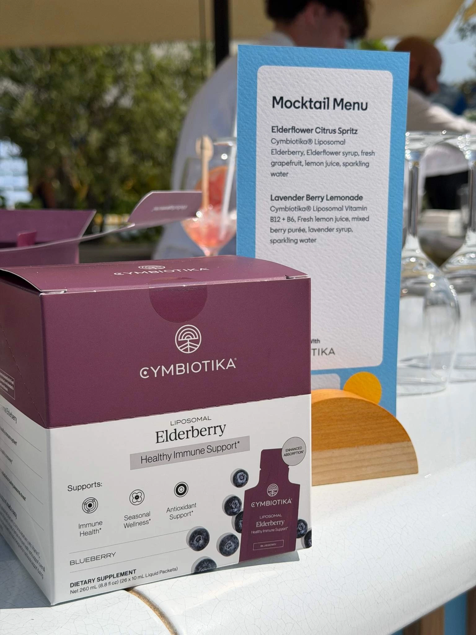 Cymbiotika Liposomal Elderberry Healthy Immune Support supplement next to a mocktail menu.