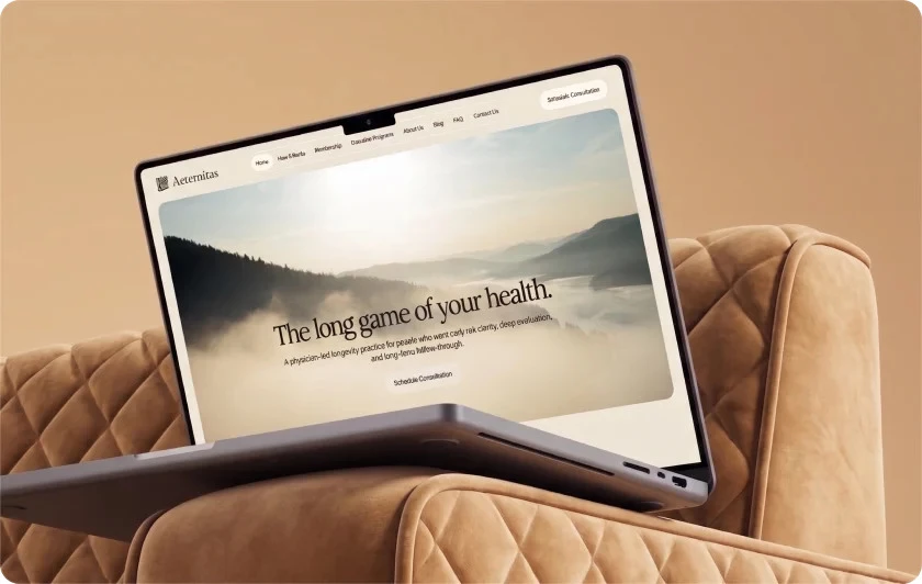 Aeternitas Launches New Website Alongside Premier Marketing's PPC Campaign A laptop resting on a tan couch displays the Aeternitas homepage, showing a foggy mountain landscape with the tagline "The long game of your health" and a Schedule Consultation button.