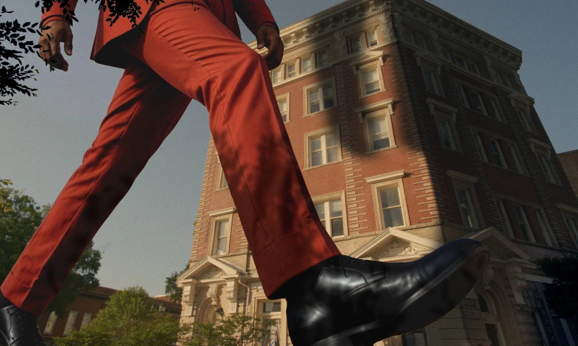 A larger-than-life figure in a red suit walking passed a building.