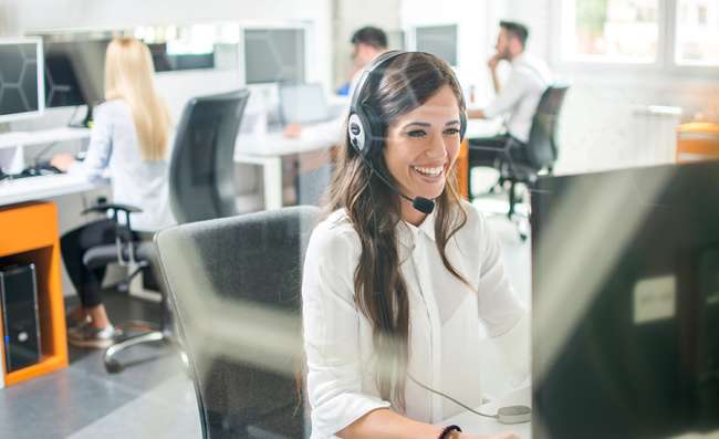 Smiling woman with headphones at a computer providing answering services