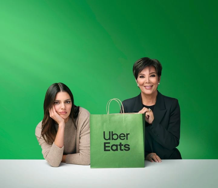 Uber Eats Ad with Kendall and Kris Jenner Kendall frowns as Kris smiles holding green bag with Uber Eats logo