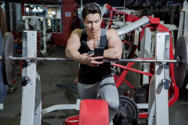 man-leaning-on-gym-equipment-with-phone Man leaning on gym equipment with phone