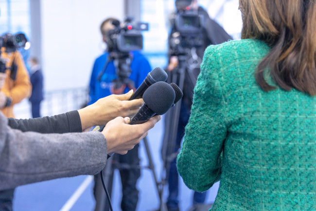 Journalists hold their mics out to interview a woman