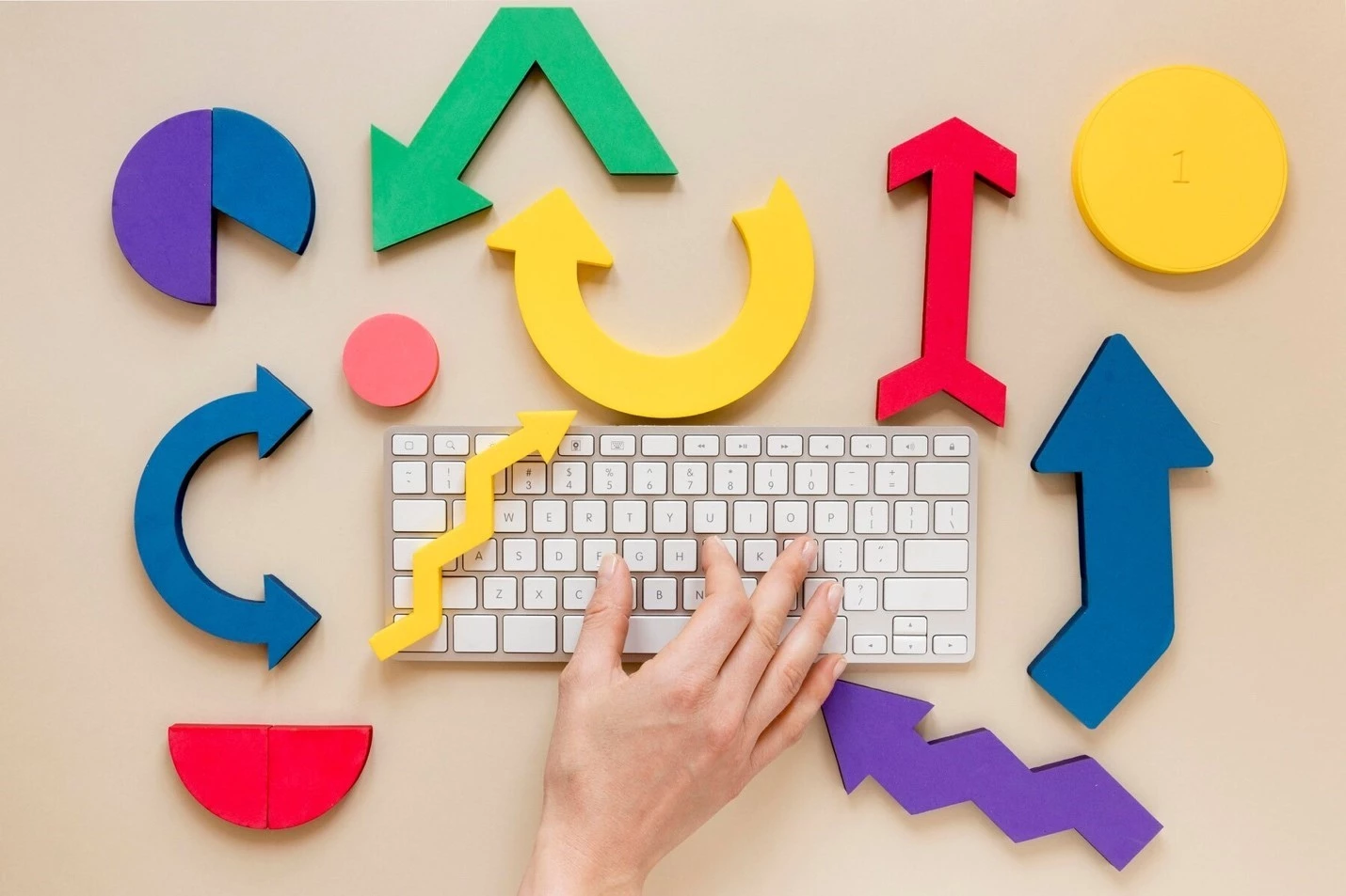A person's right hand resting on a keyboard. There are various wooden cut-outs of geometric shapes.