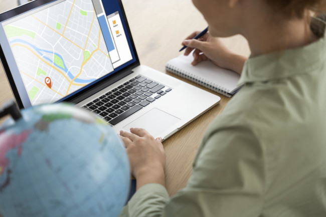 A woman looks at a map on her laptop while holding a pen