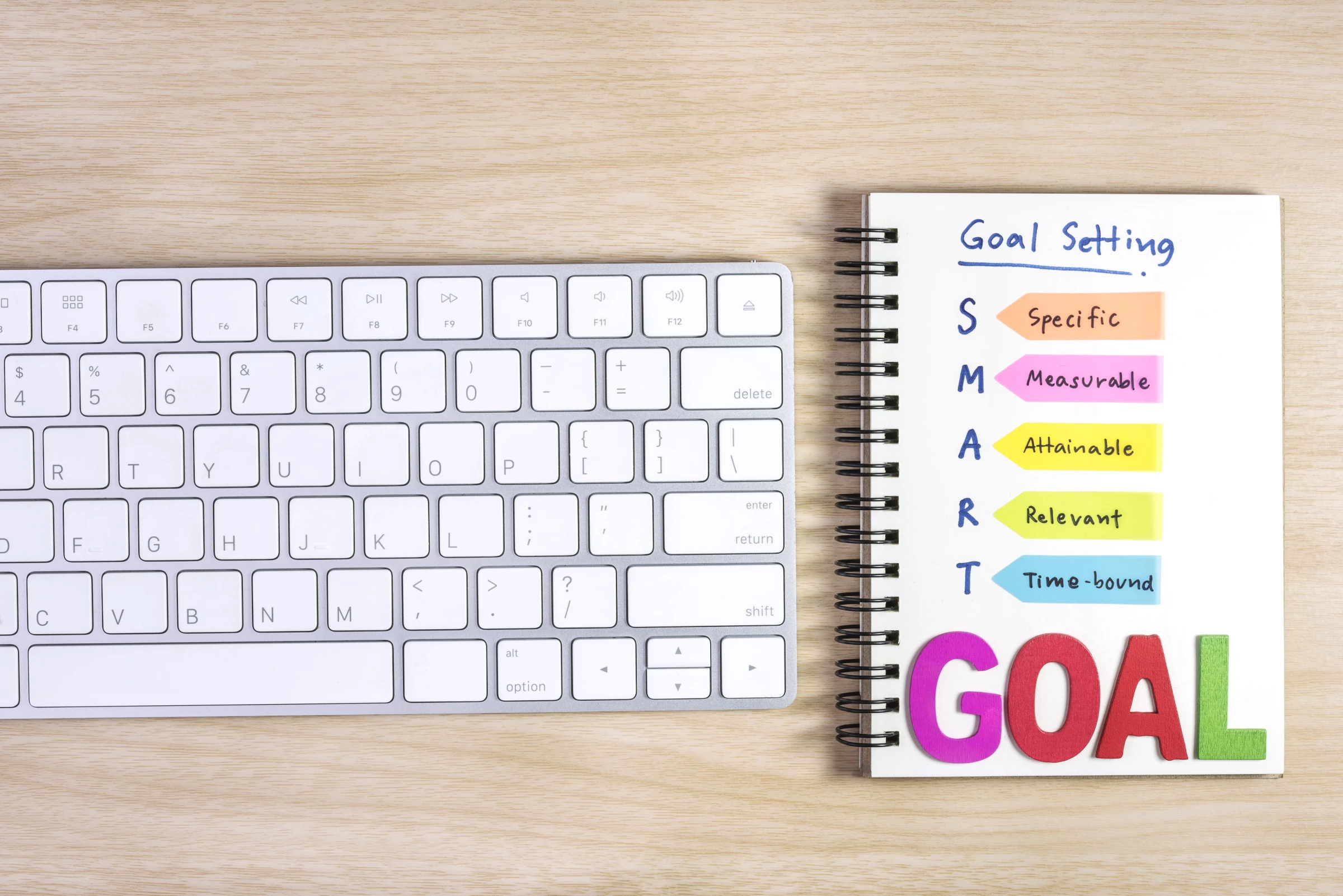 A computer keyboard with a notebook that says “smart goal”