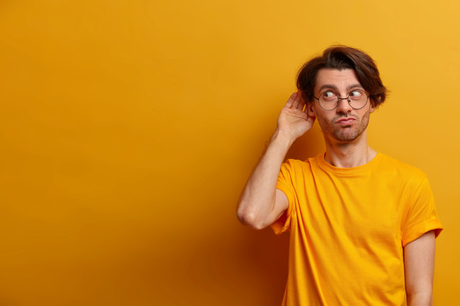 A man in an orange shirt cups his ear to listen