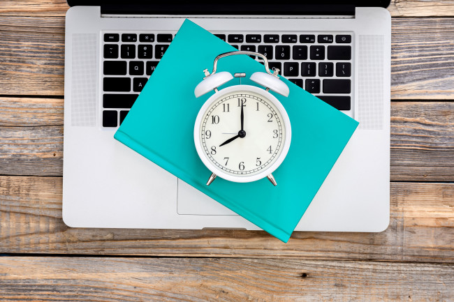 Alarm clock on a notebook placed on a laptop, concept of email scheduling