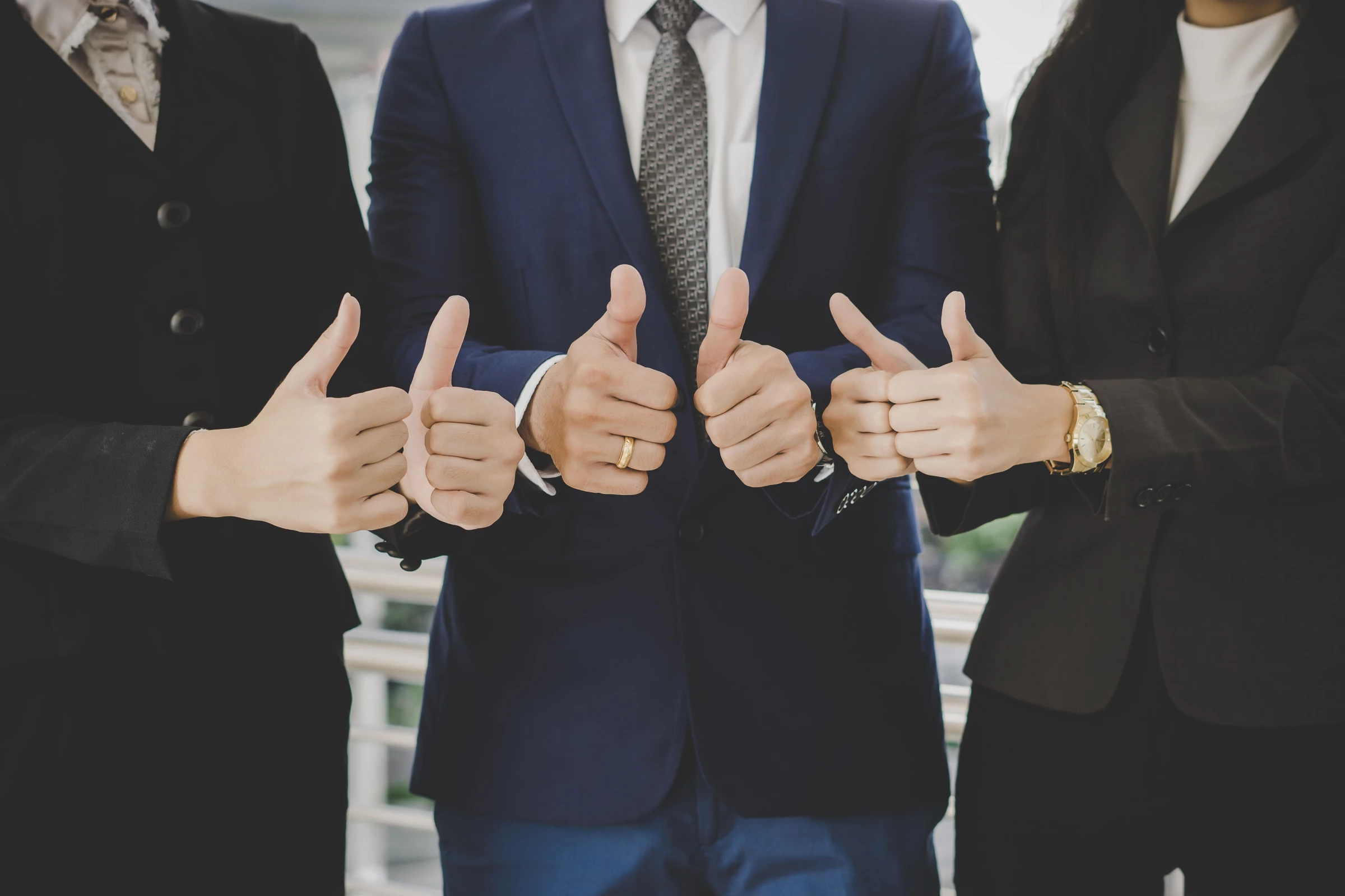 Business team in formal attire giving thumbs-up.
