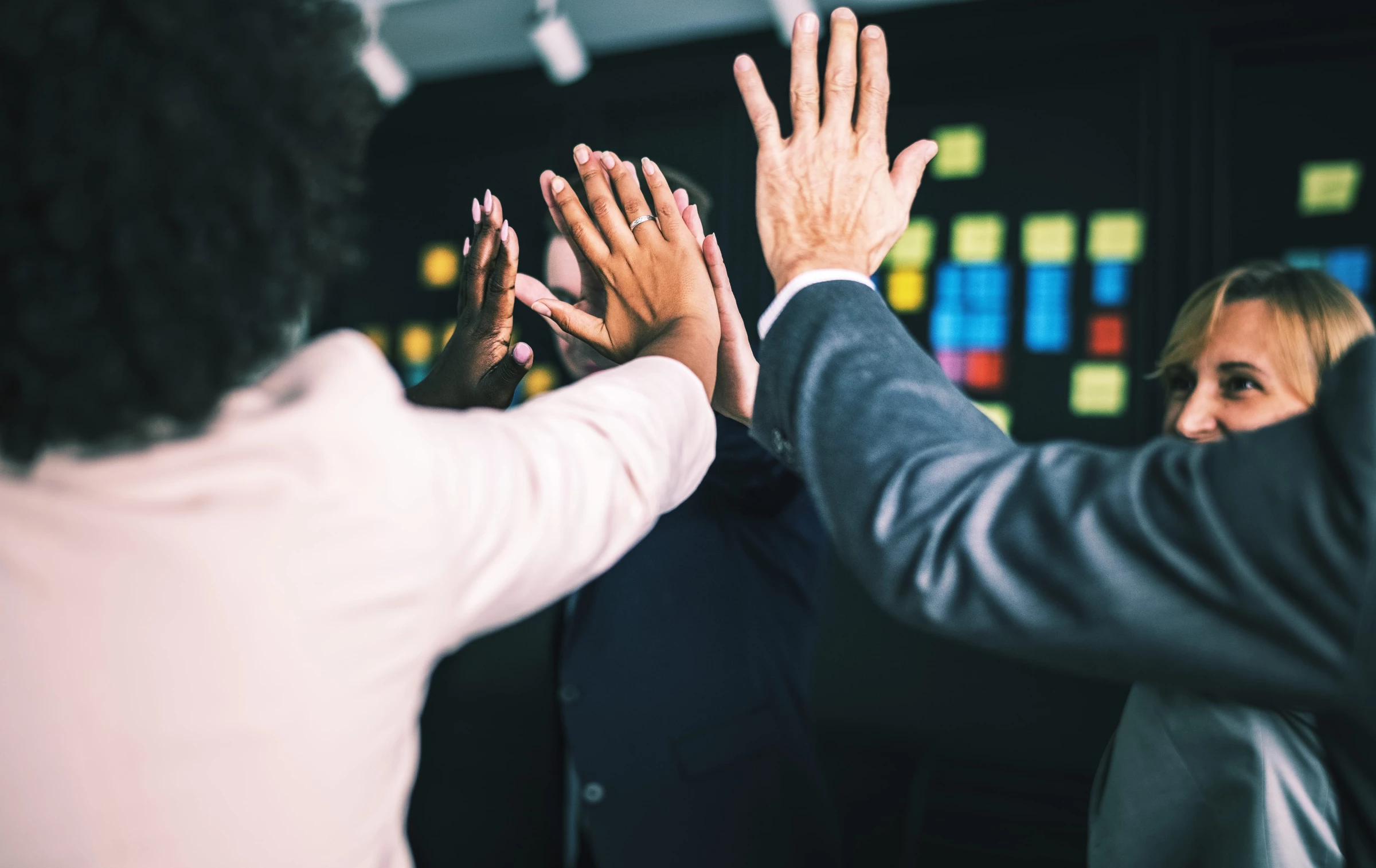 Team celebrating with a group high five in front of a planning board.