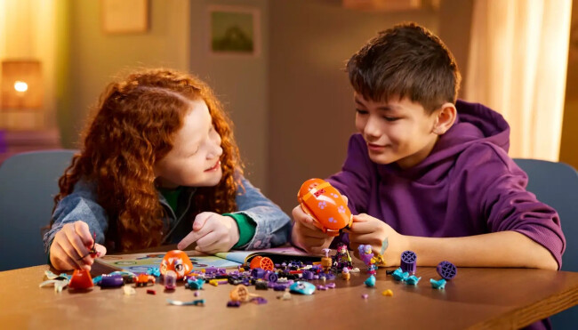 Two children smiling and playing with colorful LEGO pieces at a table.