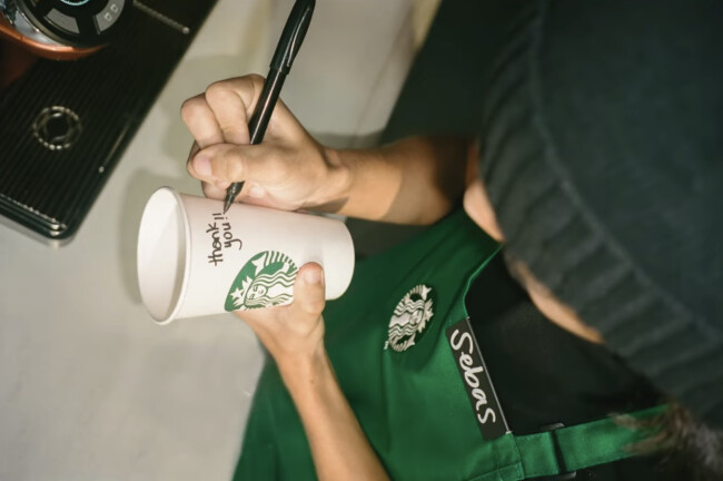 A barista writing on a Starbucks cup in "Together" | Source: Starbucks A barista writing on a Starbucks cup in "Together" | Source: Starbucks
